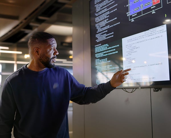 A man pointing at a huge screen filled with programming codes and schematics.