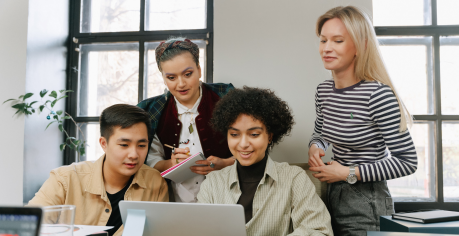 Postgraduate students huddled around a student with a laptop.