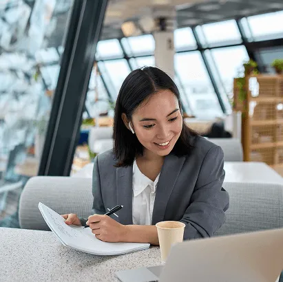 Professional seated at a table, working with documents and a laptop.