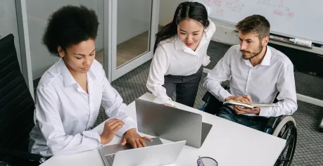 Three people in an office setting looking at laptop screens. 