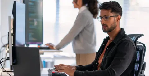 A cybersecurity analyst with eyeglasses working on a laptop.
