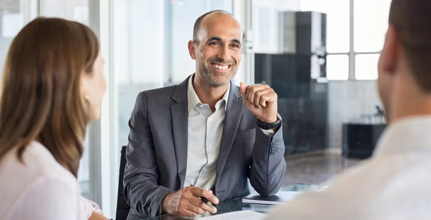 An analyst meets with two coworkers at a conference table.