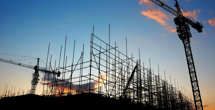 Construction site featuring cranes and scaffolding against a clear sky, indicating active building work in progress.