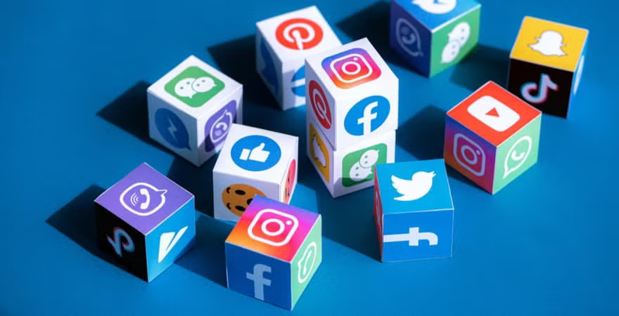 Colorful cubes featuring popular social media app icons such as Facebook, Instagram, Twitter, TikTok, Snapchat, and YouTube are scattered on a blue surface.