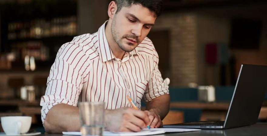 Adult man sitting in a cafe taking notes on an assignment for his master's degree